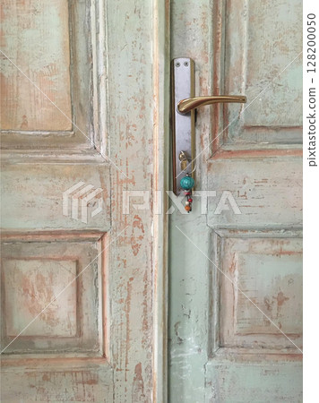 Weathered wooden door with faded pastel paint, featuring a brass handle and a key with a turquoise bead keychain. Weathered wooden door with faded pastel paint, featuring a brass handle and a key with a turquoise bead keychain. 128200050