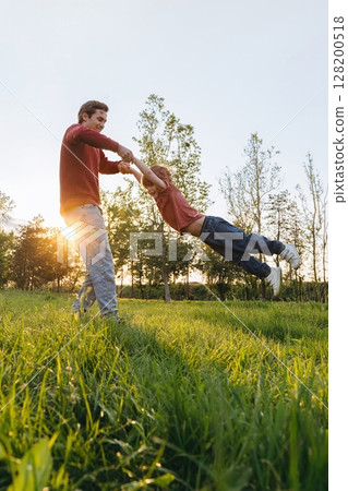 Father spinning son in park at sunset Father spinning son in park at sunset 128200518