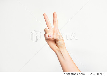 Woman's hand gesturing peace sign or victory on light grey background. Woman's hand gesturing peace sign or victory on light grey background. 128200703