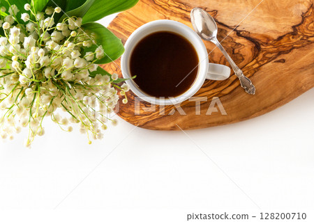 Cup of coffee and fresh bouquet of blooming lily of valley flowers on wooden stand on white background. Top view, flat lay, copy space. Cup of coffee and fresh bouquet of blooming lily of valley flowers on wooden stand on white background. Top view, flat lay, copy space. 128200710