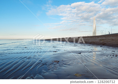Beautiful sunrise on beach of park St. Petersburg is 300 years old on Gulf of Finland. Calm smooth water with cirrus clouds reflected, St. Petersburg, Russia 128200712