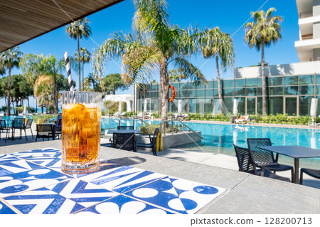 Fresh alcoholic cocktail with ice in glass on swimming pool. Hard strong drink on sunlight with palms. Concept summer luxury holiday and travel 128200713