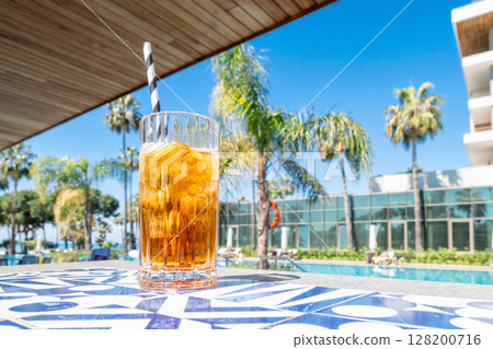 Fresh alcoholic cocktail with ice in glass on swimming pool. Hard strong drink on sunlight with palms. Concept summer luxury holiday and travel Fresh alcoholic cocktail with ice in glass on swimming pool. Hard strong drink on sunlight with palms. Concept summer luxury holiday and travel 128200716