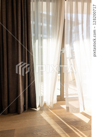 Modern room interior with an open window in minimal style. Transparent tulle with morning sun rays on shadow background. Vertical photo. Modern room interior with an open window in minimal style. Transparent tulle with morning sun rays on shadow background. Vertical photo. 128200717