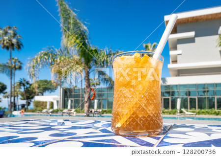 Fresh alcoholic cocktail with ice in glass on swimming pool. Hard strong drink on sunlight with palms. Concept summer luxury holiday and travel Fresh alcoholic cocktail with ice in glass on swimming pool. Hard strong drink on sunlight with palms. Concept summer luxury holiday and travel 128200736