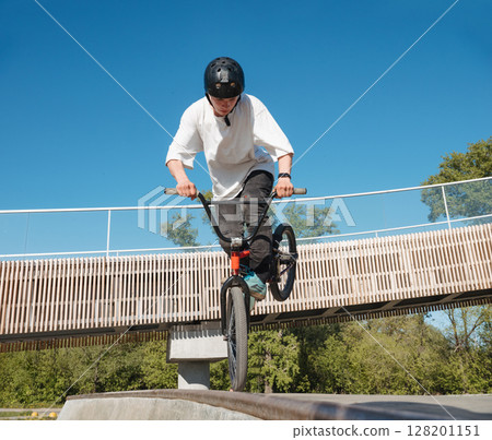 Skilled BMX rider performing Footjam trick in ramp park. Young BMX bicycle rider having fun and posing in Footjam outdoors. Footjam trick is front wheel stand. Concrete ramp street park Skilled BMX rider performing Footjam trick in ramp park. Young BMX bicycle rider having fun and posing in Footjam outdoors. Footjam trick is front wheel stand. Concrete ramp street park 128201151