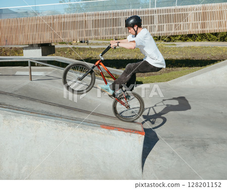 Skilled BMX rider performing Manual trick in ramp park. Young BMX bicycle rider having fun and posing in Manual Wheelie riding outdoors. Riding in back wheel in street park. Concrete street park Skilled BMX rider performing Manual trick in ramp park. Young BMX bicycle rider having fun and posing in Manual Wheelie riding outdoors. Riding in back wheel in street park. Concrete street park 128201152