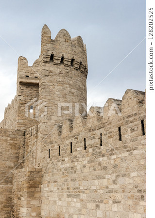 Ancient stone fortress walls featuring a textured round tower under a blue sky 128202525
