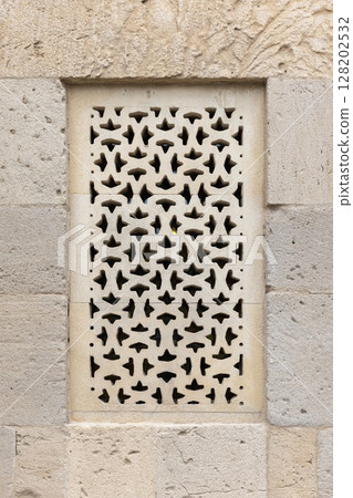 Intricately carved stonework featuring a geometric perforated window design 128202532