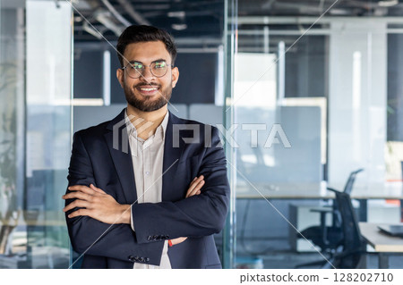 Confident mature man businessman posed in a office setting with arms folded. The image exudes professionalism, confidence, and ambition, making it ideal for business or leadership-related contexts. 128202710