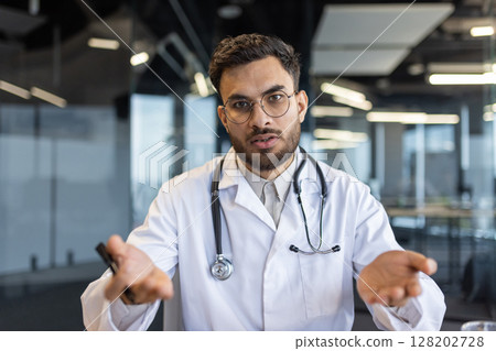 Doctor talking to camera during an online video call. Telehealth and telemedicine are modern means for doctor-patient interaction from remote locations Doctor talking to camera during an online video call. Telehealth and telemedicine are modern means for doctor-patient interaction from remote locations 128202728