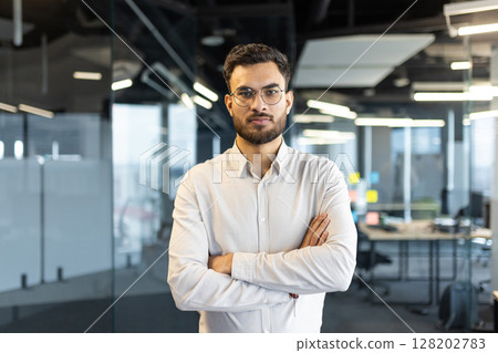 Mature man businessman confidently stands with arms crossed in a modern office environment. The subject portrays professionalism, ambition, and determination, epitomizing a successful corporate image 128202783