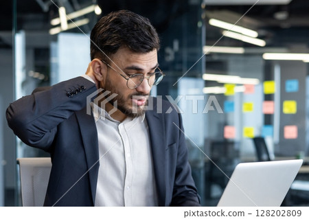Overtired and overworked man at workplace inside office in business suit. Businessman suffering from severe neck pain. 128202809