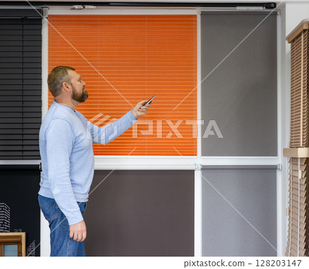 Man Operating Motorized Window Blinds in Sunshade Showroom Man Operating Motorized Window Blinds in Sunshade Showroom 128203147