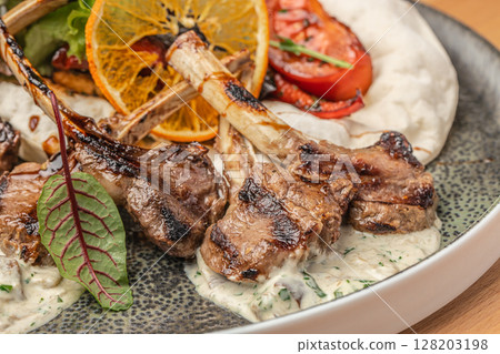 Grilled lamb chops served on a creamy herb sauce with roasted vegetables, flatbread, and a slice of dried orange for garnish Grilled lamb chops served on a creamy herb sauce with roasted vegetables, flatbread, and a slice of dried orange for garnish 128203198