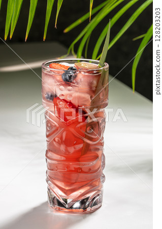 A vibrant red cocktail served in a decorative tiki glass, garnished with fresh strawberries, blueberries, and a green leaf for a tropical and refreshing presentation A vibrant red cocktail served in a decorative tiki glass, garnished with fresh strawberries, blueberries, and a green leaf for a tropical and refreshing presentation 128203203