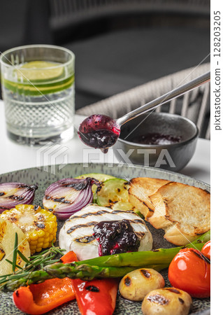 A gourmet platter featuring grilled vegetables, creamy baked camembert topped with berry sauce, and toasted bread, served with a refreshing drink for a perfect combination of flavors and textures 128203205