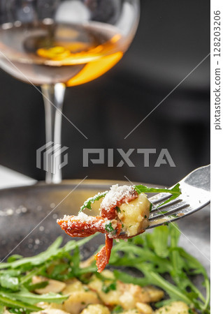 A close-up of a gourmet bite of gnocchi with sun-dried tomatoes, fresh arugula, and grated parmesan, paired with a glass of white wine for an elegant dining experience A close-up of a gourmet bite of gnocchi with sun-dried tomatoes, fresh arugula, and grated parmesan, paired with a glass of white wine for an elegant dining experience 128203206
