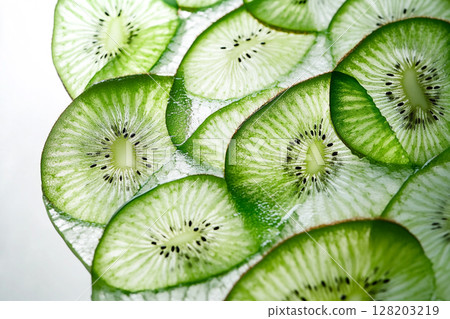 A close-up view of numerous vibrant green kiwi slices, showcasing their intricate patterns of seeds and fibrous texture against a white background. 128203219