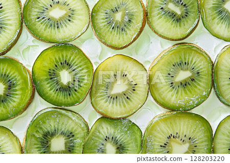 A close-up view of numerous vibrant green kiwi slices, showcasing their intricate patterns of seeds and fibrous texture against a white background. 128203220