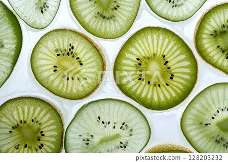 A close-up view of numerous vibrant green kiwi slices, showcasing their intricate patterns of seeds and fibrous texture against a white background. 128203232