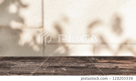 Soft leaf shadows fall on a tiled wall behind a rustic wooden table, evoking a calm, sunlit atmosphere perfect for quiet moments or natural product displays 128203339