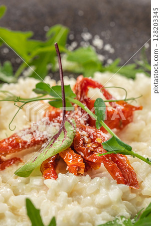 A close-up of creamy risotto topped with sun-dried tomatoes, parmesan cheese, and fresh green herbs, showcasing vibrant colors and rich textures 128203345