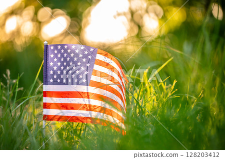 A small American flag rests quietly in the soft golden light of a peaceful summer sunset, Independence Day or traveling in America concept 128203412