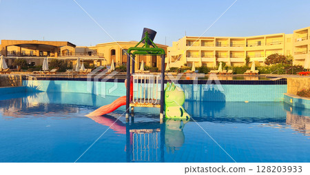 A colorful water slide and play area in a resort pool under a clear blue sky. The setting is in Egypt by the Red Sea during summer. A colorful water slide and play area in a resort pool under a clear blue sky. The setting is in Egypt by the Red Sea during summer. 128203933