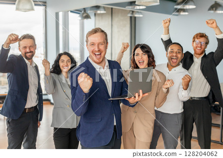 A group of diverse business professionals celebrates a successful project in their modern office. The team is ecstatic, with smiles and raised fists, expressing their shared joy. 128204062