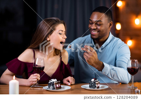Romantic Mixed Couple Dining In Restaurant, Eating Desserts And Drinking Wine, Celebrating Anniversary Or Valentine's Day Together. Loving Black Man Feeding His Girlfriend With Cake, Free Space Romantic Mixed Couple Dining In Restaurant, Eating Desserts And Drinking Wine, Celebrating Anniversary Or Valentine's Day Together. Loving Black Man Feeding His Girlfriend With Cake, Free Space 128204089