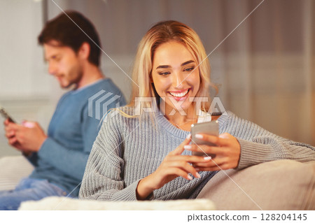 Cheating. Unfaithful Girlfriend Chatting On Phone With Lover Sitting Next To Boyfriend On Couch Indoor. Selective Focus Cheating. Unfaithful Girlfriend Chatting On Phone With Lover Sitting Next To Boyfriend On Couch Indoor. Selective Focus 128204145