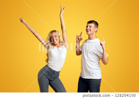 Youth concept. Portrait of joyful millennial guy and girl dancing in studio over yellow background. 128204150