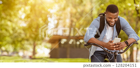 Outdoor portrait of smiling young afro man with mobile phone in the street, sitting on bike, downloading music playlist, riding to work 128204151