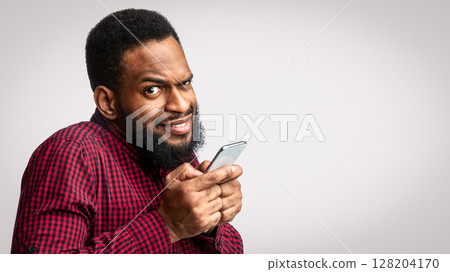 Phone Fraud. Suspicious Black Man Using Smartphone Looking At Camera Posing Over White Studio Background. Telephone Phreaking And Cellphone Scam Concept 128204170