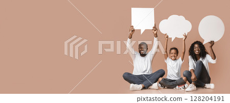 Diverse thoughts. Happy African american family of three holding empty speech bubbles over heads sitting on floor, yellow background with free space. Diverse thoughts. Happy African american family of three holding empty speech bubbles over heads sitting on floor, yellow background with free space. 128204191