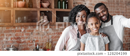 Happy african family taking selfie at kitchen, wearing aprons and smiling 128204199