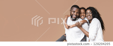 Family love. Happy african american parents posing with their little daughter, laughing together and looking at camera over yellow background 128204205