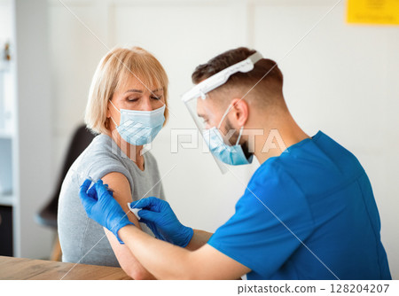 Coronavirus prevention and treatment concept. Senior female patient getting vaccinated against covid-19 at clinic. Young medic making antiviral vaccine injection to mature woman 128204207