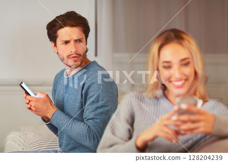 Cheating. Jealous Husband Noticed Wife Texting On Cellphone Suspecting Infidelity At Home. Selective Focus Cheating. Jealous Husband Noticed Wife Texting On Cellphone Suspecting Infidelity At Home. Selective Focus 128204239