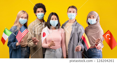 International relations, student exchange and education during COVID-19 epidemic. Young multi ethnic people in protective masks holding flags of countries, isolated on orange background, copy space International relations, student exchange and education during COVID-19 epidemic. Young multi ethnic people in protective masks holding flags of countries, isolated on orange background, copy space 128204261