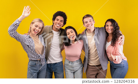 Education at university or college abroad. Cheerful young multiracial international students have fun, laughing, hugging and waving to camera isolated on orange background, copy space, studio shot 128204316