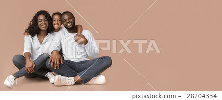 Family Time. African American Parents And Daughter Sitting On Floor And Posing to Camera Over Yellow Studio Background Family Time. African American Parents And Daughter Sitting On Floor And Posing to Camera Over Yellow Studio Background 128204334