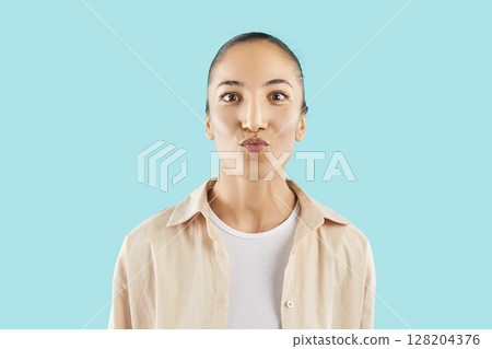 Young woman posing with kiss face expression on studio blue background and looking at camera. 128204376