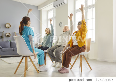 Nurse guiding elderly patients through seated exercises for mobility and wellness in nursing home. 128204407