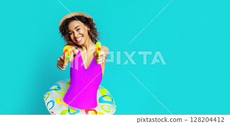 A young African American woman wearing a swimsuit and a straw hat smiles and holds two water guns, sitting inside an inflatable ring. She is ready to have fun in the water. A young African American woman wearing a swimsuit and a straw hat smiles and holds two water guns, sitting inside an inflatable ring. She is ready to have fun in the water. 128204412