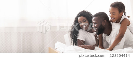 African american family of three using laptop while lying on bed together, browsing internet or watching movie 128204414