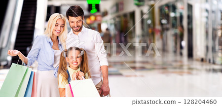 A happy family of three strolls through a shopping mall, with the mother carrying shopping bags and the daughter holding onto her own bags, panorama with copy space A happy family of three strolls through a shopping mall, with the mother carrying shopping bags and the daughter holding onto her own bags, panorama with copy space 128204460