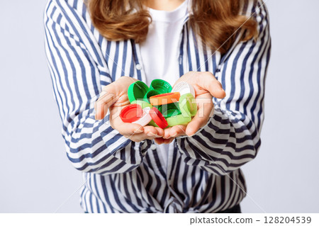 A woman is actively engaging in recycling by holding a collection of colorful plastic bottle caps in her hands. Her eco-friendly approach reflects awareness for environmental sustainability. 128204539