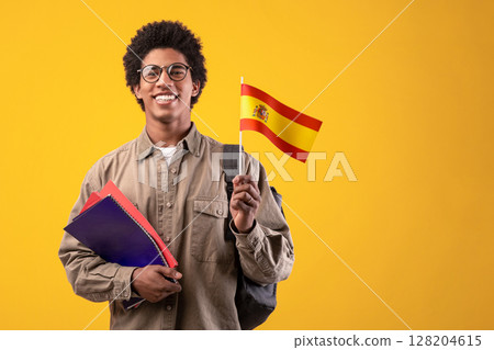 Learning new language, education and travel. Young smiling african american male in glasses with backpack hold notebooks and small Spain flag, isolated on beige background, studio shot, empty space Learning new language, education and travel. Young smiling african american male in glasses with backpack hold notebooks and small Spain flag, isolated on beige background, studio shot, empty space 128204615